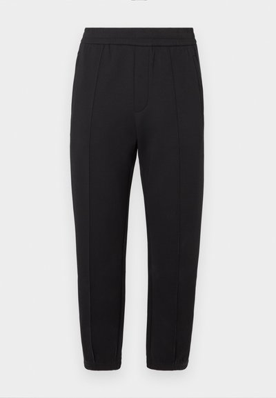 Čierne teplákové nohavice s elastickým pásom, zúženým strihom, prednými záhybmi, bočnými vreckami a elastickými lemy pri členkoch.