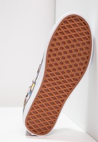 Basket de sport à semelle en caoutchouc avec une semelle extérieure texturée marron, une semelle intermédiaire blanche et un design imprimé coloré présentant divers personnages sur le dessus.