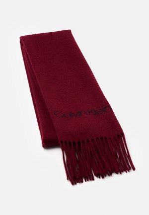 Złożony bordowy szalik z frędzlami na końcach i czarnym haftowanym logo "Calvin Klein" w pobliżu krawędzi na białym tle.