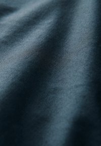 Tessuto blu scuro con una texture liscia, leggermente lucida e un sottile motivo a costine, che crea delicati avvallamenti sulla sua superficie.