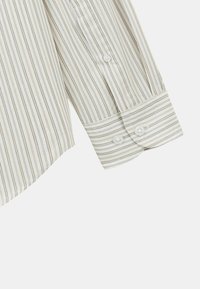 Chemise rayée en tissu léger avec de fines rayures verticales beige et grises. Les poignets ont deux fermetures à bouton et un ourlet arrondi.