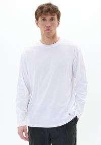 Witte katoenen t-shirt met lange mouwen en een ronde hals, met een klein geprint label aan de zoom en een gladde textuur.