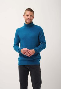 Maglione turtleneck turchese con una consistenza morbida, polsini e fondo a costine. La vestibilità è rilassata, abbinata a jeans scuri.