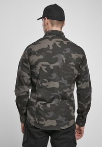 Kamuflage skjorte med et mønster i mørkegrå og khaki, med knaplukning fortil og lange ærmer, set bagfra.