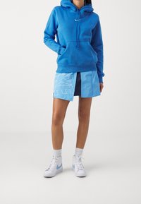 Blå huvtröja med framficka och snörning, i kombination med en ljusblå kjol med en djärv vit logotyp, och vita hög-top sneakers.