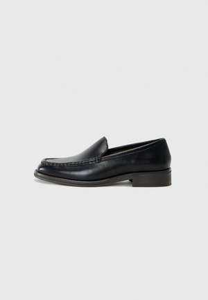 Zwarte leren herenslof met gestikte moc toe, lage houten hak en slip-on ontwerp op een effen lichte achtergrond.