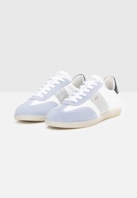 Baskets bleu clair et blanches en matériaux suede et cuir. Les caractéristiques incluent des lacets, un embout arrondi, des accents argentés et une semelle beige.