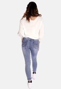 Blusa bianca leggera abbinata a jeans skinny azzurri. I jeans presentano cuciture sottili sulle tasche posteriori. Il modello indossa sneaker bianche.