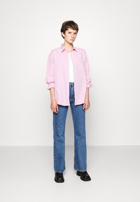 Rood-witte gestreepte longsleeve shirt, met knoopsluiting aan de voorkant, gecombineerd met lichtblauwe rechte spijkerbroek en zwarte enkellaarzen.