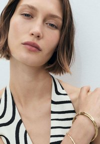 Gold bangles on a wrist, with a black and white striped halter top. Focus on features: smooth texture and contrasting colors.