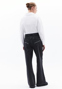 Jeans negros de pierna ancha con dobladillo deshilachado y dos bolsillos traseros. Combinados con una camisa blanca de manga larga, con el cabello recogido en un moño.