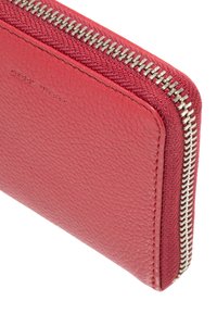 Rdeča usnjena denarnica z teksturiranim zaključkom. Ima srebrno zadrgo ob robu in subtilno embosirano oznako. Minimalističen dizajn.