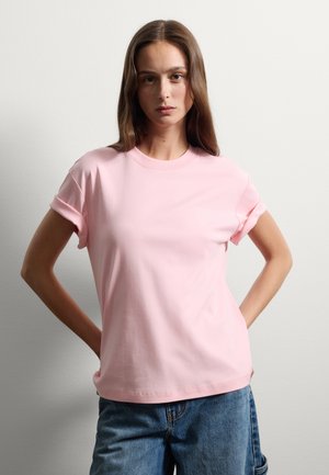 T-shirt di cotone rosa chiaro con scollatura rotonda e maniche arrotolate, abbinato a jeans di denim larghi. Tessuto morbido, vestibilità casual.