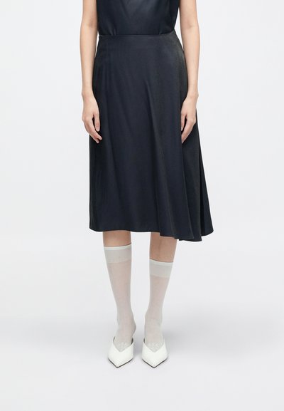 Črna midi krila iz gladkega materiala, v kombinaciji s prosojnimi, svetlo sivimi nogavicami in belimi čevlji z ostrim nosom. Preprost, eleganten dizajn.