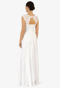 Robe en dentelle blanche avec des manches courtes, un dos en trou de serrure et une taille smockée. La jupe se déploie élégamment jusqu'aux chevilles.