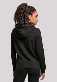 Zwarte hoodie met een trekkoordkap, ribbelboorden en -zoom. Zachte stoftextuur. Draagt samen met zwarte leggings, die een ontspannen pasvormontwerp tonen.