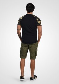 T-shirt noire à manches courtes en camouflage, associée à un short cargo kaki. Design décontracté avec une coupe ajustée et des accents contrastés.