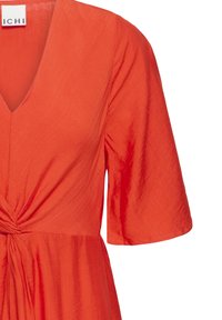 Robe orange à manches courtes avec col en V et détail de nœud torsadé à la taille, confectionnée dans un tissu léger et texturé.