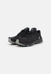 Baskets de sport noires avec tige en mesh, accents réfléchissants, système de laçage élastique et semelle extérieure en caoutchouc gris durable.