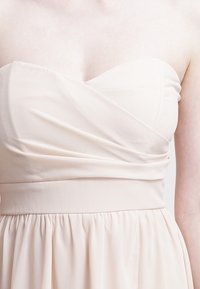 Robe bustier en tissu beige doux, avec un corsage drapé à fronces et une jupe évasée. Texture lisse avec une taille ajustée.