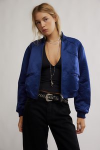 Modrá bomber bunda s hladkou texturou, vroubkovanými manžetami a kapsami, doplněná černým topem a černými kalhotami s vysokým pasem a pásem.
