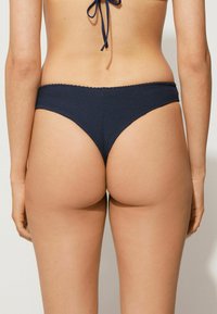 Tmavě modré bikiny s texturovaným, žebrovaným designem. Střih je vysoký s minimálním pokrytím a na pase je elastický pás.