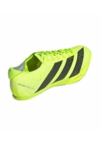 Bright yellow athletic shoe with black stripes, textured knit upper, and lightweight design. Features sharp studs for grip on the sole.
