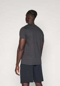 Tricou scurt, gri închis, dintr-un material neted, cu decolteu rotund și detalii minime de coasere. Purtați cu pantaloni scurți bleumarin.