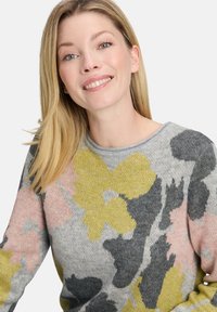Sweter dzianinowy z szarym tłem i wielokolorowym kwiatowym wzorem w odcieniach żółtego, różowego i czarnego. Gładka tekstura i okrągły dekolt.
