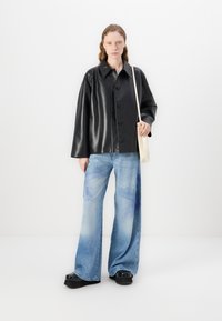Chaqueta de cuero sintético negra con grandes botones, combinada con jeans de pierna ancha azul claro con patrones de acuarela, y zapatos de plataforma negros.