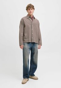 Brown checkered button-up shirt with a front pocket, paired with faded blue jeans and beige slip-on shoes, set against a plain background.