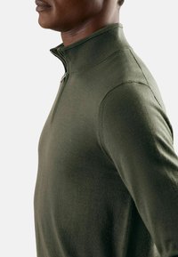 Donkergroen pullover trui met een kwart rits, gemaakt van glad gebreid materiaal, met een hoge kraag en aansluitende lange mouwen.