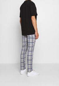 Lyhythihainen musta t-paita yhdistetty harmaisiin ruudullisiin housuihin, joissa on sinisiä ja valkoisia raitoja. Valkoiset tennarit viimeistelevät asun.