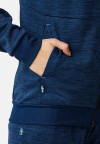 Marineblaues Hoodie aus strukturiertem Stoff. Mit Kängurutasche und gerippten Bündchen. Enthält kleine Akzente mit der schwedischen Flagge an Tasche und Saum.
