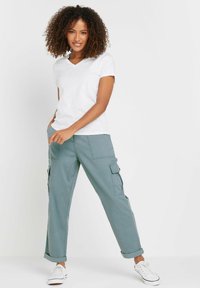 Witte V-hals t-shirt gecombineerd met relaxed-fit, lichtgroene cargobroek met zijzakken en opgerolde zoom. Draagt met witte sneakers.