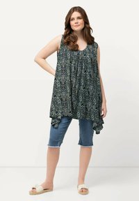 Mouwloze tuniek in donkerblauw met een groen en crèmekleurig abstract patroon, met een gelaagd ontwerp en een gerimpelde zoom, gedragen met denimshorts.