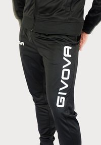 Zwart sportjack en -broek van gladde stof. 'GIVOVA'-logo in het wit op het pijpje van de broek. Slanke pasvorm, met geribbelde boorden en tailleband.