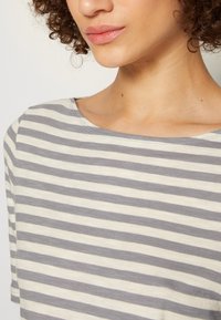 Top a rayas con franjas horizontales en gris claro y crema, material de algodón suave y un diseño de cuello ancho.