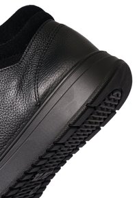 Black leather shoe heel with textured rubber sole and padded collar, shown at an angled close-up on a white background.