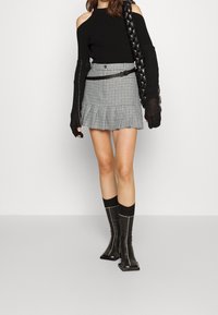 Zwarte geribbelde off-shoulder trui, geruite minirok met een rucheszoom, zwarte riem en kniehoge zwarte laarzen met vierkante neuzen en stiksel details.