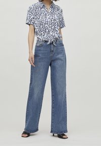 Camicetta a maniche corte con bottoni, caratterizzata da una stampa leopardata blu e nera, abbinata a jeans in denim blu a vita alta e gamba larga.