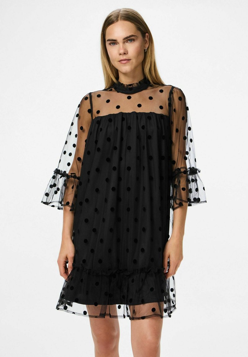 Crna haljina s točkicama, prozirni sloj, nabranim dekolteom i zvonastim rukavima. Tkanina ima zaigrani uzorak točkica i slojeviti rub.