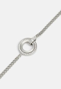 Bracciale in argento con un charm circolare decorato con cristalli trasparenti e un dettaglio del clasp con marchio.