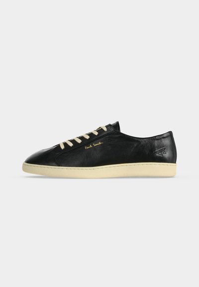 Baskets basses en cuir noir avec semelle crème et lacets, logo doré "Paul Smith" sur le côté, et symbole embossé près du talon.