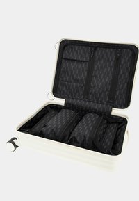 Valise rigide blanche avec un intérieur noir, dotée de plusieurs compartiments zippés et de sangles d'organisation. Roues lisses pour une mobilité aisée.