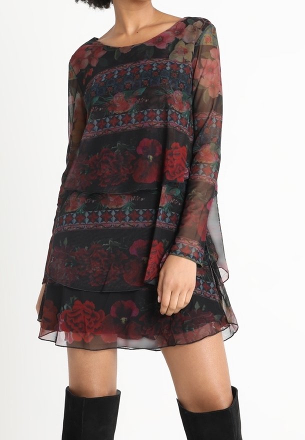 Femme portant une robe noire transparente à fleurs avec manches longues et jupe à volants, associée à des bottes noires montant aux genoux.