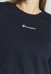 Felpa blu marina in misto cotone con scollo rotondo e un piccolo logo "Champion" bianco sul petto, texture liscia.
