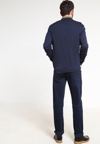 Mörkblå tröja med rund halsringning, ribbade ärmavslut och fåll, ihop med mörkblå byxor och svarta ankelstövlar. Slät textur.