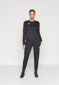 Μαύρο αθλητικό φούτερ και παντελόνι, φτιαγμένα από λεία ύφασμα, με λευκά διακριτικά λογότυπα adidas και στα δύο κομμάτια, με άνετη εφαρμογή.