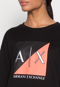 Svart sweatshirt i bomull med en framsidan grafisk design som har en korallfärgad triangel och vit text "A/X Armani Exchange."